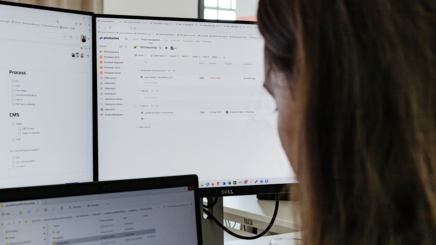 looking over a project manager's shoulder at their three computer screens showing tools for project management (Photo)